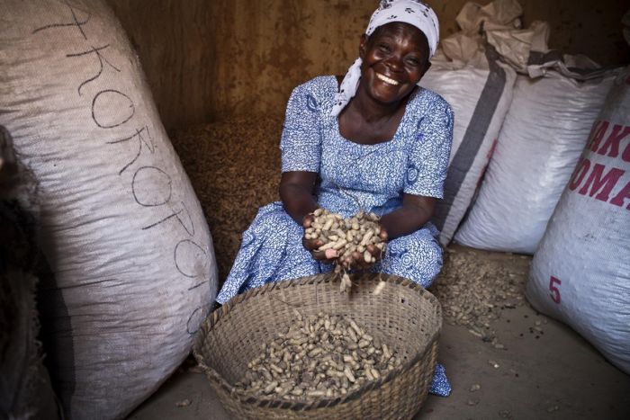 Fati, a farmer from northern Ghana, sits smiling with her harvest 